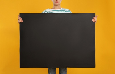 Photo of Woman holding black blank poster on yellow background, closeup. Mockup for design