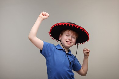 Cute boy in Mexican sombrero hat dancing on grey background