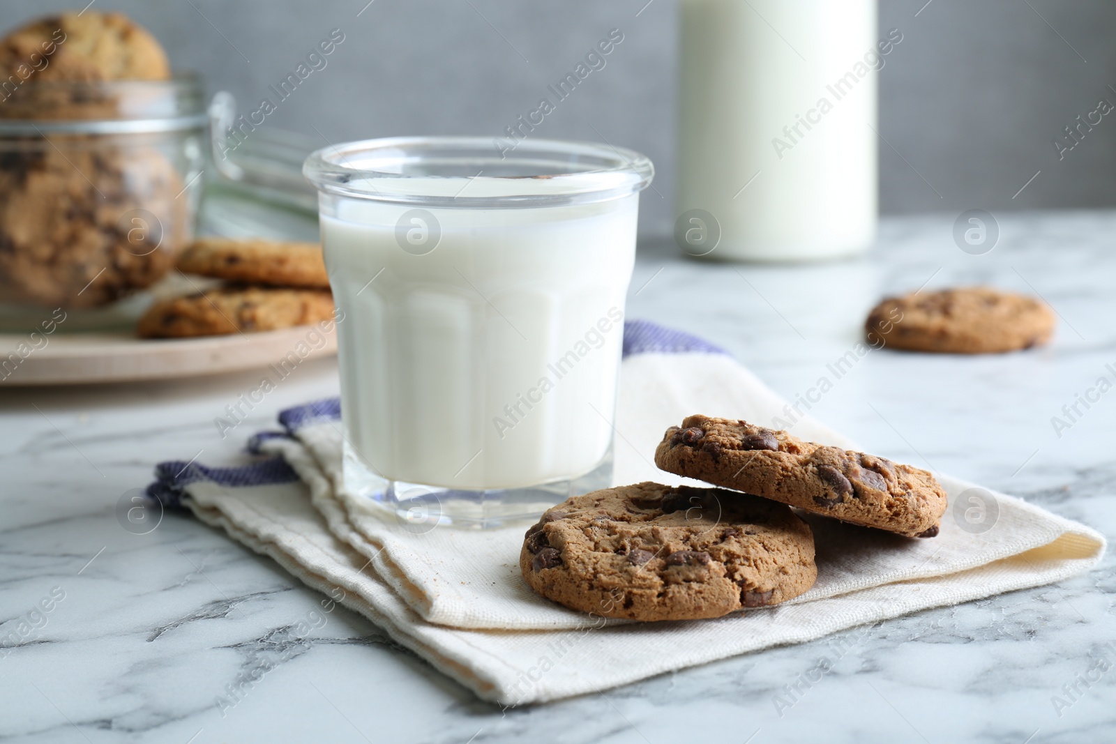 Photo of Tasty chocolate chip cookies and glass of milk on white marble table, closeup