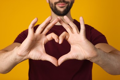 Photo of Man making heart with hands on yellow background, closeup