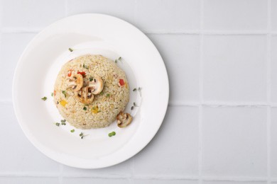 Delicious bulgur with vegetables, mushrooms and microgreens on white tiled table, top view. Space for text