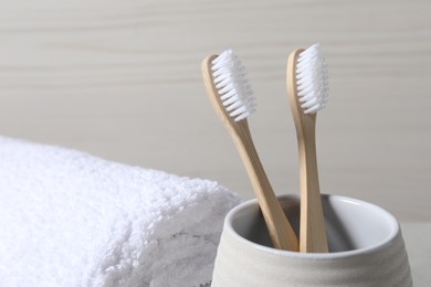 Photo of Bamboo toothbrushes in holder and soft towel on light background, closeup