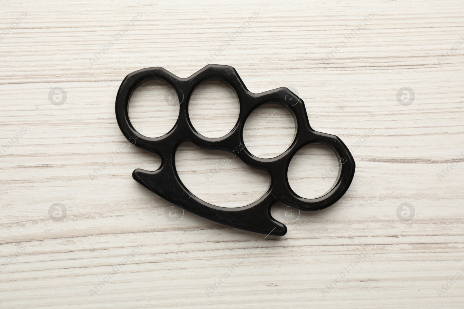 Photo of Black brass knuckles on white wooden background, top view