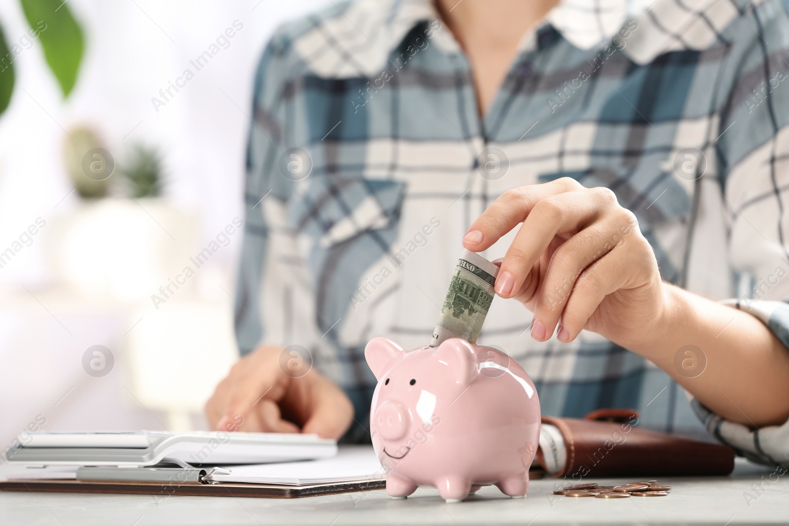 Photo of Woman putting money into piggy bank at table indoors, closeup