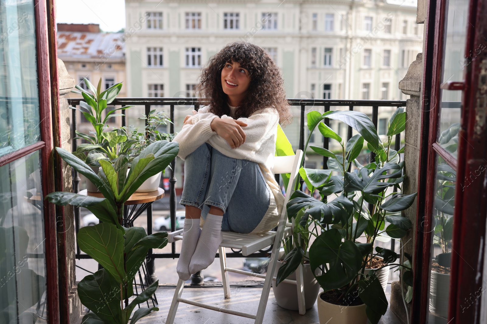 Photo of Beautiful young woman relaxing in chair surrounded by green houseplants on balcony