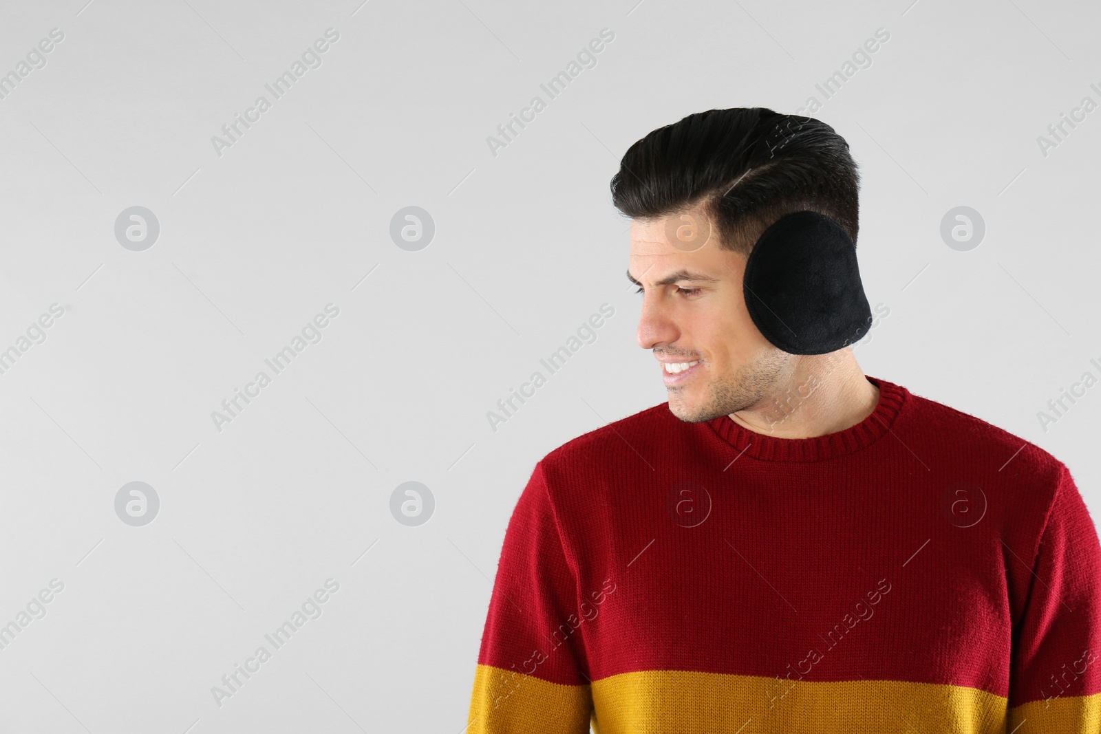 Photo of Man wearing stylish earmuffs on light background. Space for text