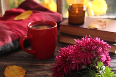 Photo of Beautiful chrysanthemum flowers, cup of hot drink and books on wooden table. Autumn still life