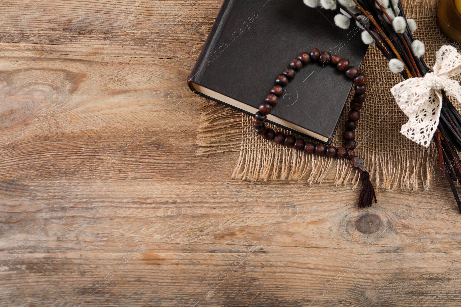 Photo of Rosary beads, Bible and willow branches on wooden table, flat lay. Space for text