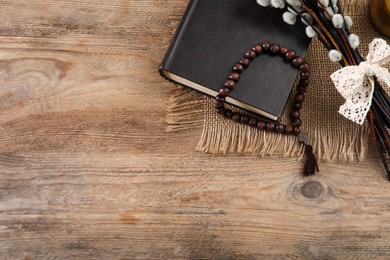 Photo of Rosary beads, Bible and willow branches on wooden table, flat lay. Space for text
