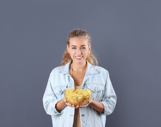 Woman with bowl of potato chips on grey background