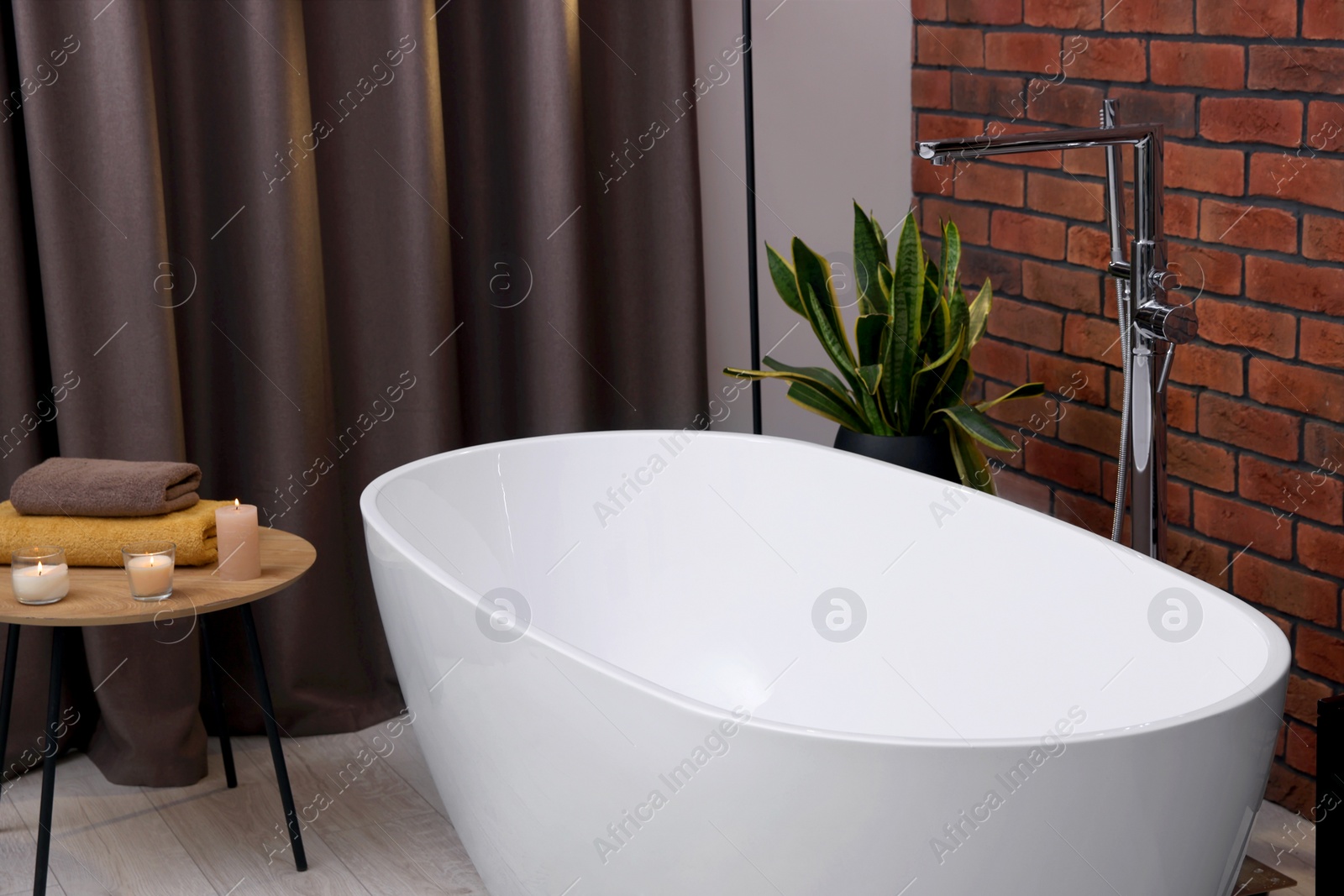 Photo of Stylish bathroom interior with ceramic tub, burning candles and terry towels on wooden coffee table