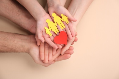 Photo of Parents and kid holding paper cutout of family with heart in hands on beige background, top view