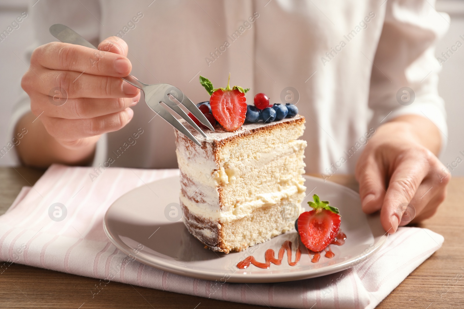 Photo of Woman eating delicious homemade cake with fresh berries at table