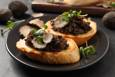 Photo of Delicious bruschettas with truffle sauce and microgreens on black table, closeup