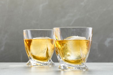 Photo of Tasty whiskey with ice in glasses on light table, closeup