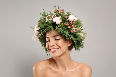 Happy young woman wearing wreath on grey background