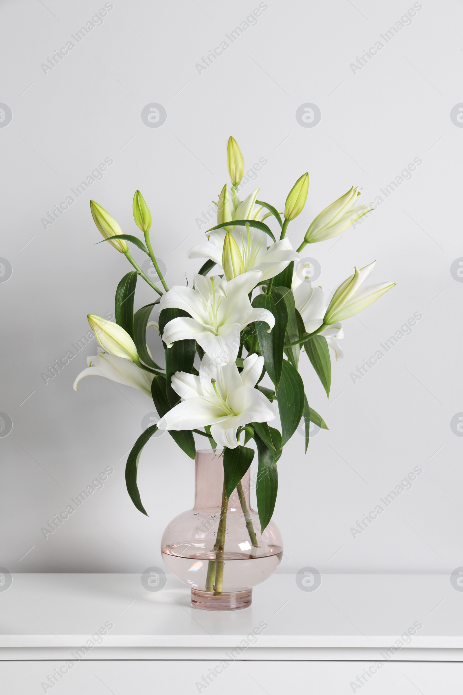 Photo of Beautiful bouquet of lily flowers in glass vase on table near white wall
