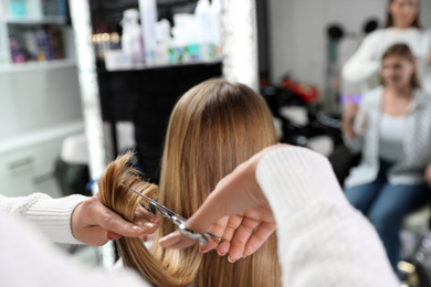 Photo of Hairdresser making stylish haircut with professional scissors in salon, closeup