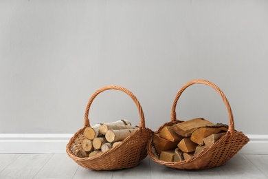 Photo of Wicker baskets with firewood near grey wall indoors, space for text