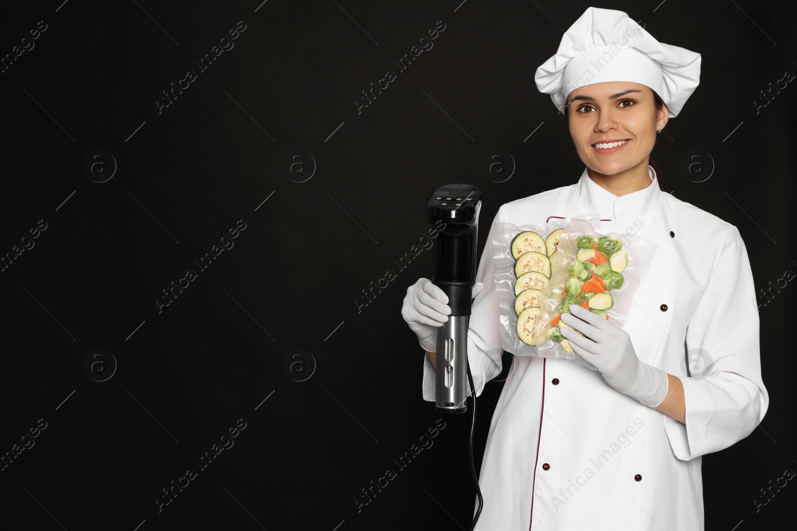 Photo of Chef holding sous vide cooker and vegetables in vacuum packs on black background. Space for text