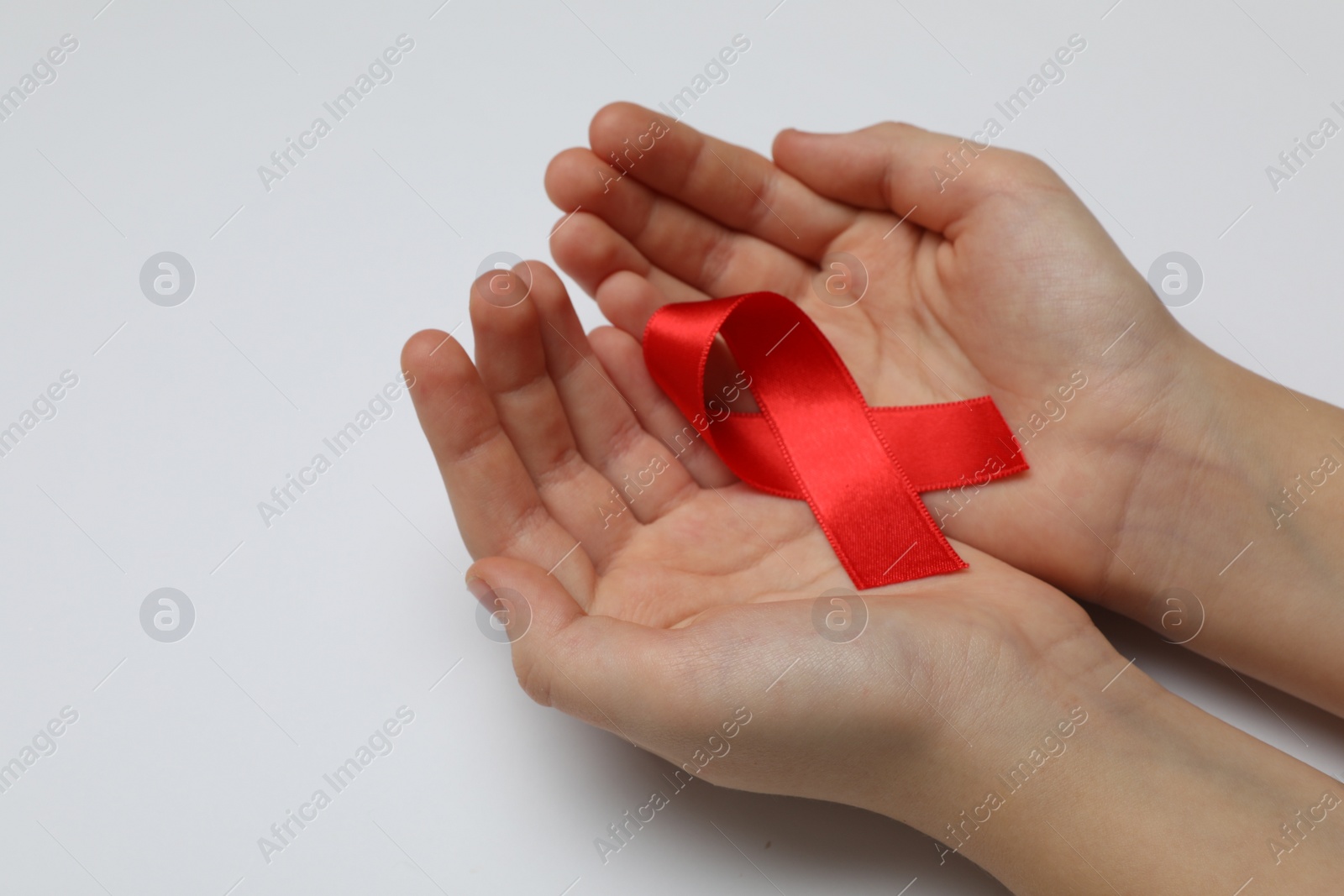 Photo of Little girl holding red ribbon on white background, closeup. AIDS disease awareness