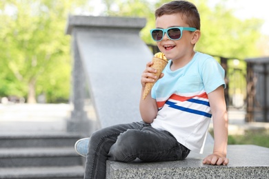 Cute little boy with delicious ice cream outdoors, space for text