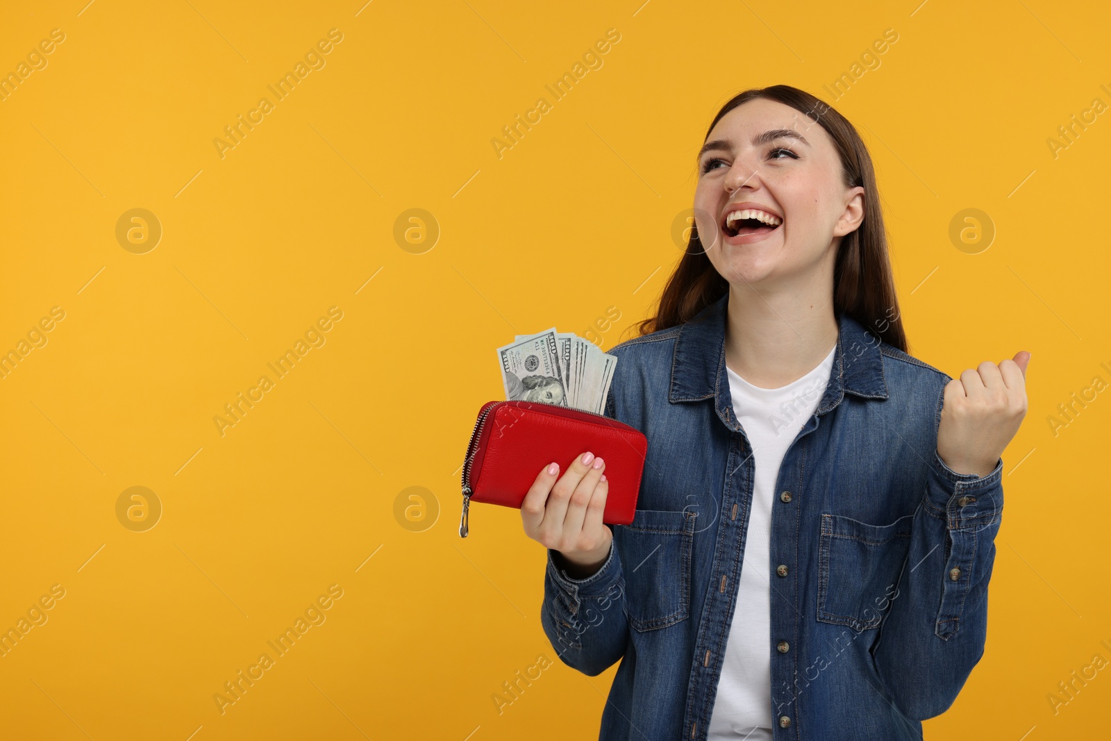 Photo of Happy woman holding wallet with dollar banknotes on orange background, space for text