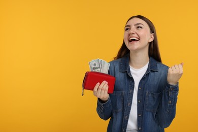 Happy woman holding wallet with dollar banknotes on orange background, space for text