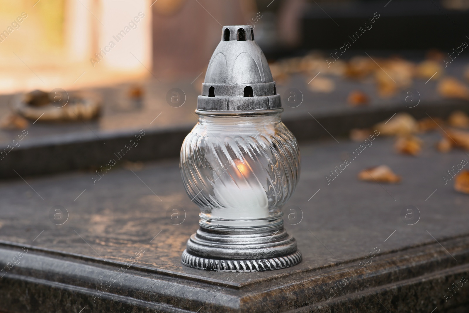 Photo of Grave lantern with burning candle on granite surface in cemetery