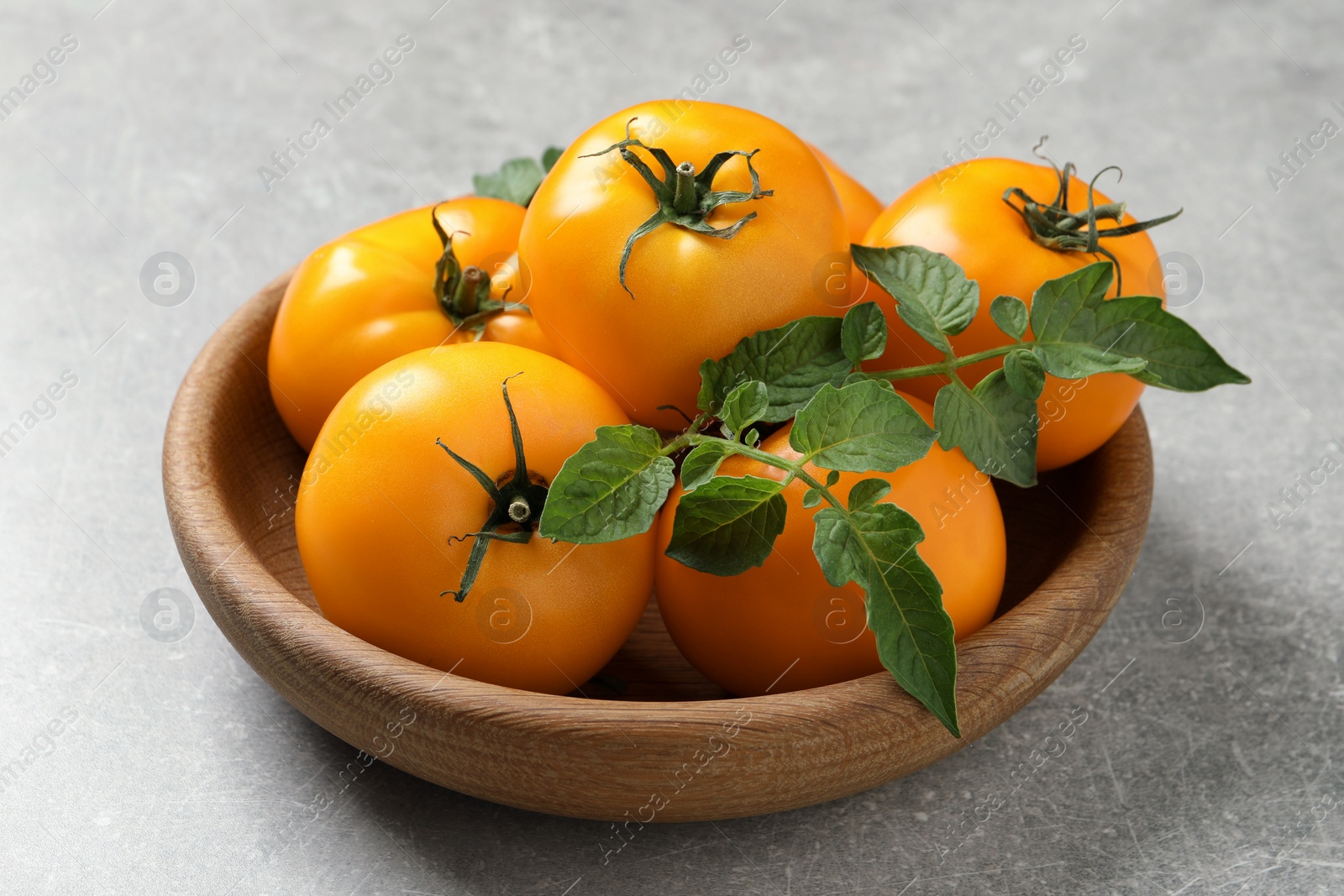 Photo of Fresh ripe yellow tomatoes with leaves on light grey table