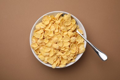 Photo of Breakfast cereal. Tasty corn flakes in bowl and spoon on brown table, top view