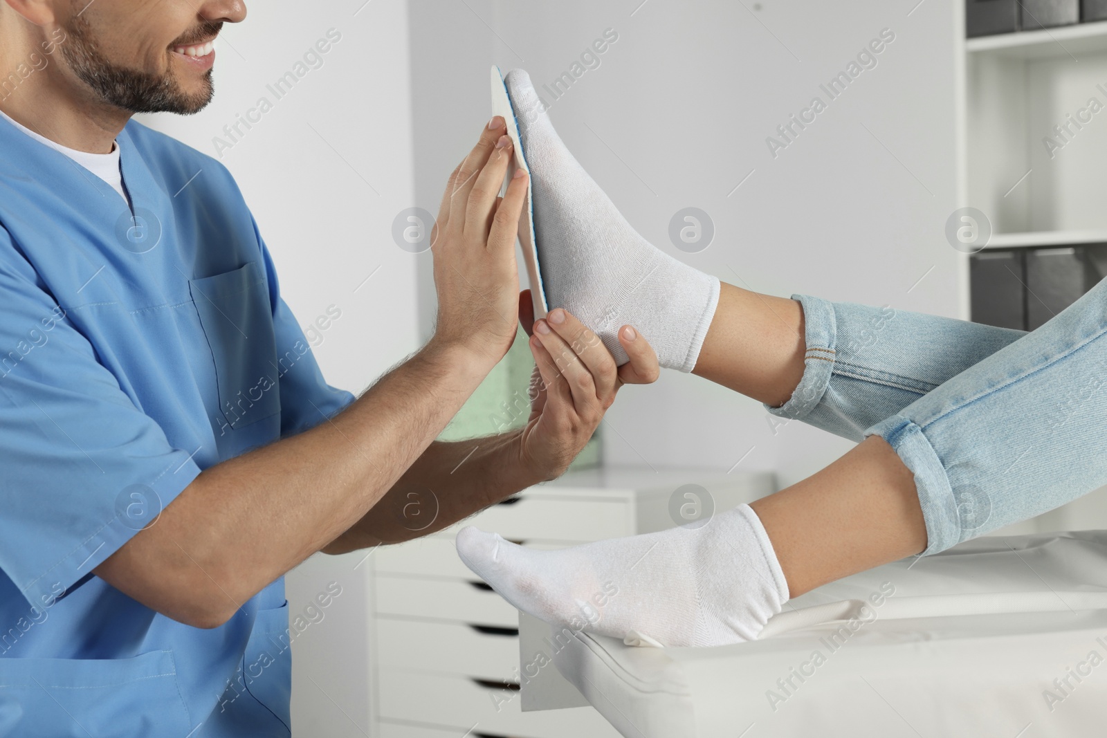 Photo of Male orthopedist fitting insole to patient's foot in hospital, closeup