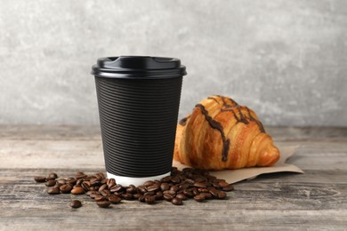 Coffee to go. Paper cup with tasty drink, croissant and beans on wooden table