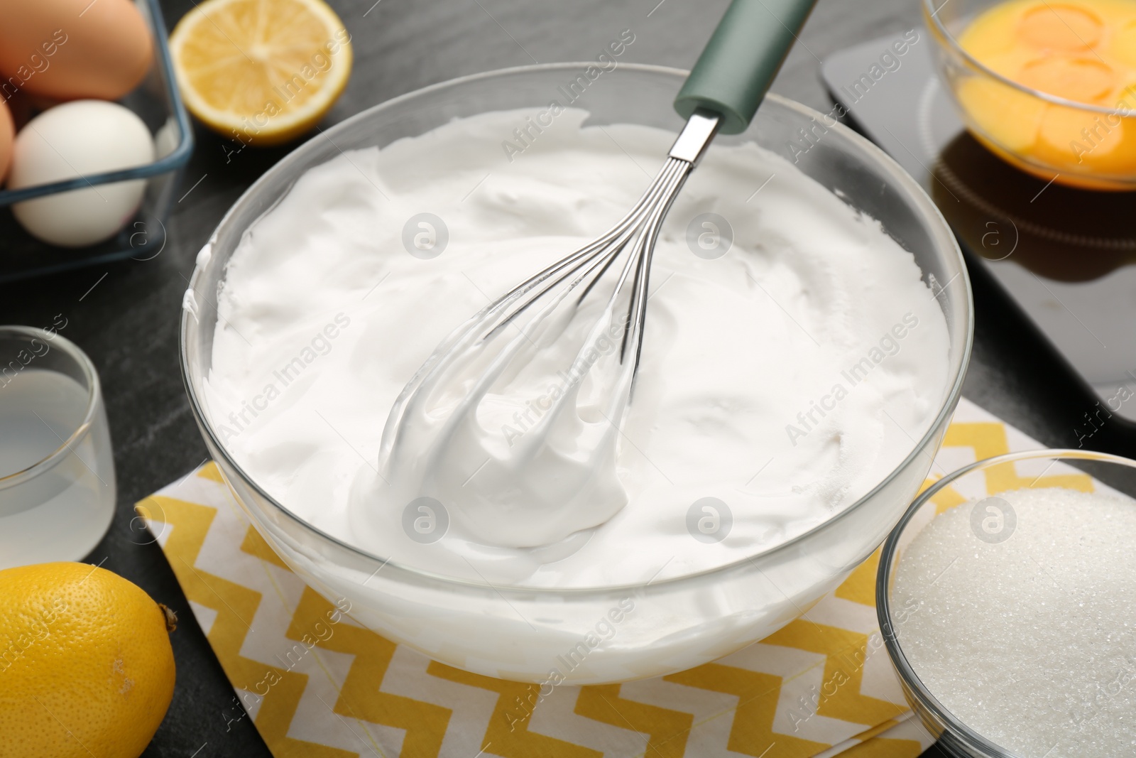 Photo of Bowl with whipped cream, whisk and ingredients on table, closeup