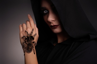 Photo of Mysterious witch with spooky spider on dark background, closeup