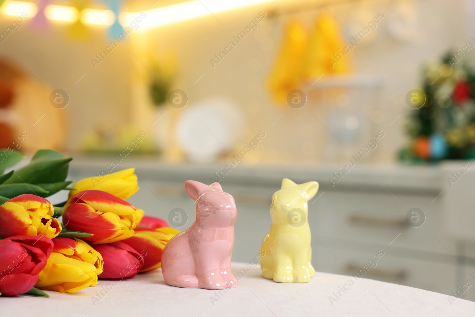 Photo of Easter decorations. Bouquet of tulips and bunny figures on white table indoors, closeup. Space for text