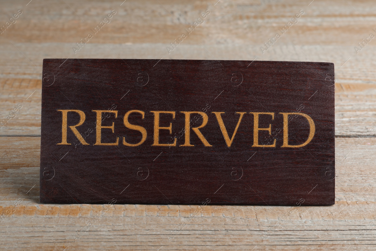 Photo of Elegant sign RESERVED on wooden surface. Table setting element