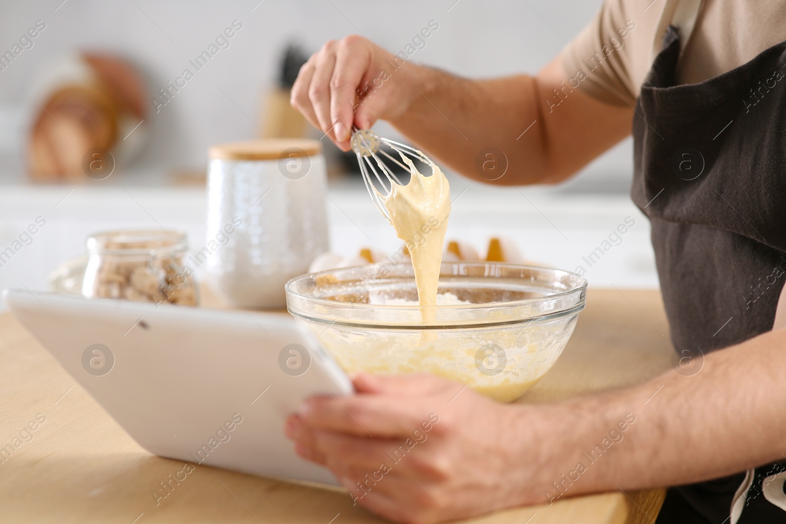 Photo of Man making dough while watching online cooking course via tablet in kitchen, closeup