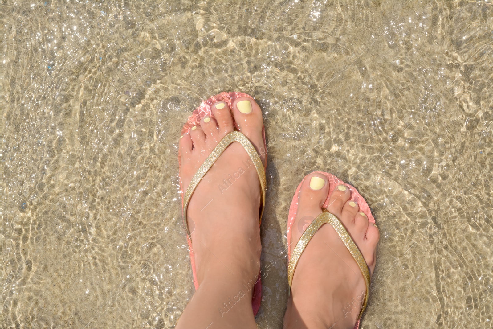 Photo of Woman wearing stylish pink flip flops standing in shallow sea water, top view