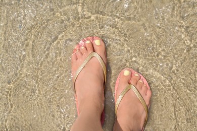 Photo of Woman wearing stylish pink flip flops standing in shallow sea water, top view