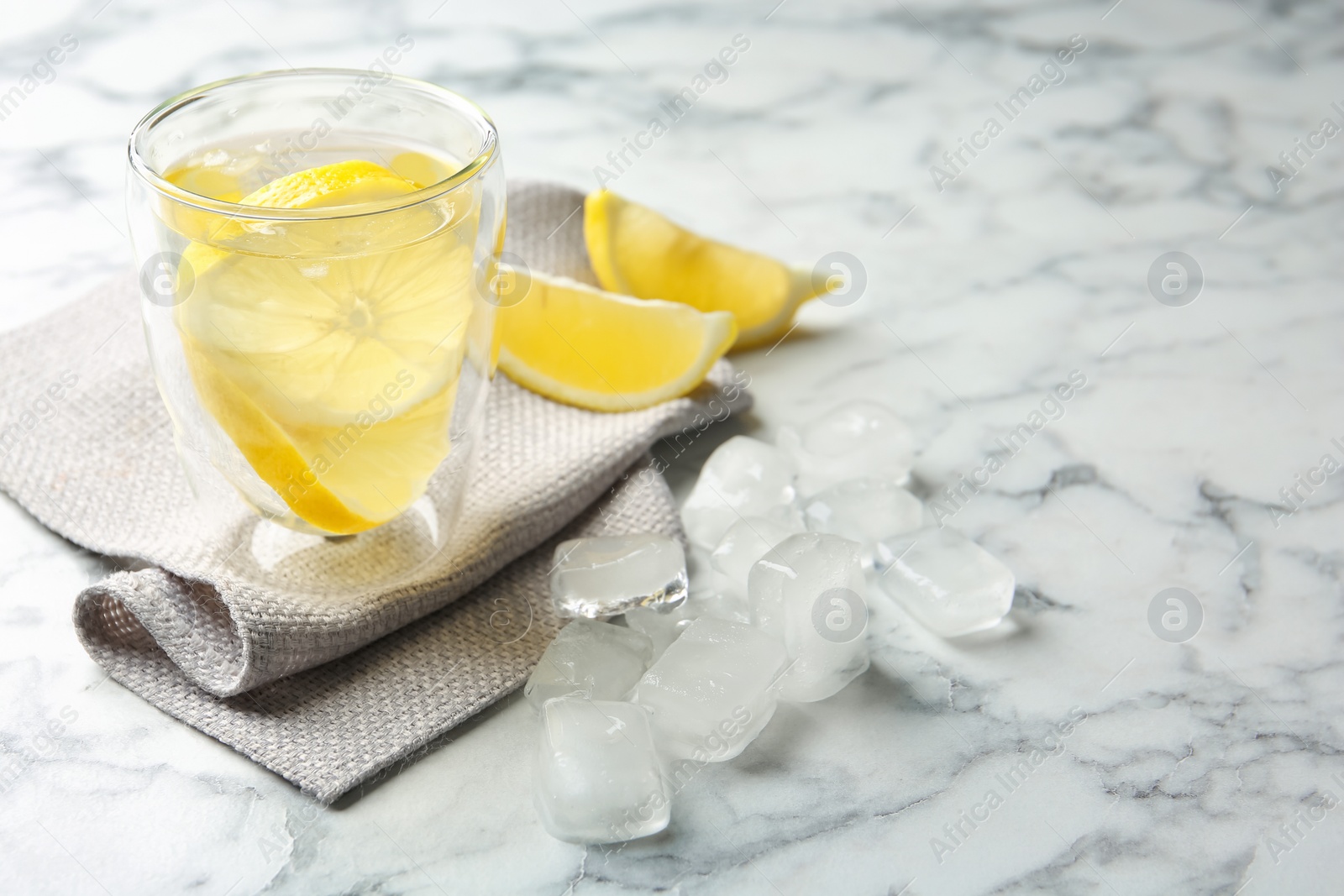 Photo of Glass with lemon water and ice cubes on marble table