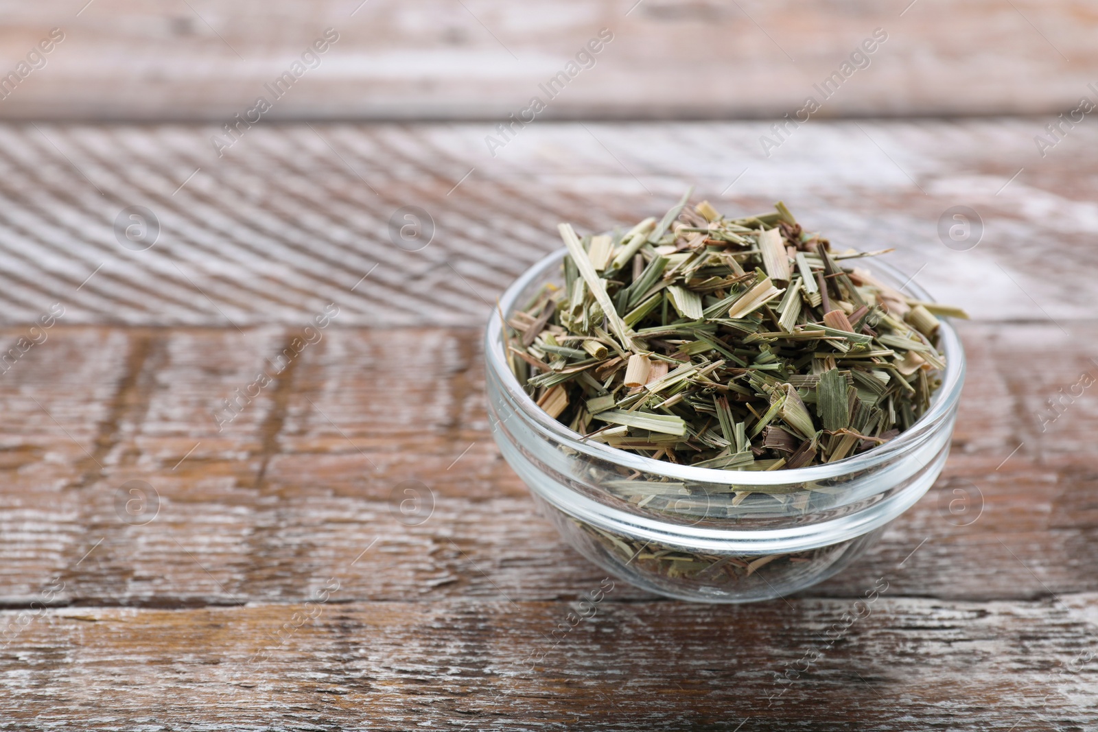 Photo of Glass bowl with aromatic dried lemongrass on wooden table. Space for text