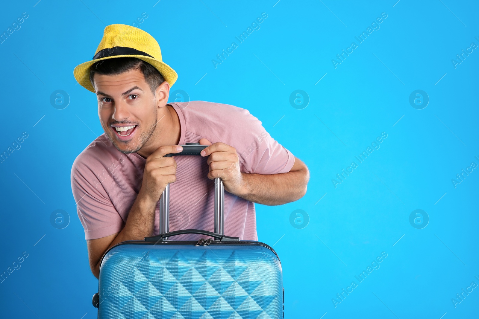 Photo of Excited man with suitcase for summer trip on blue background. Vacation travel