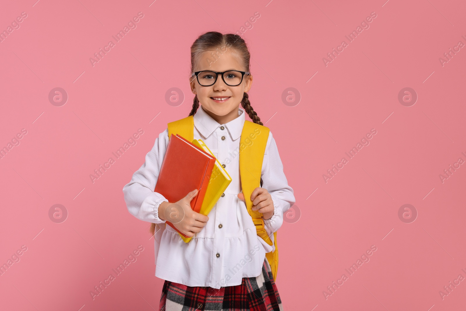 Photo of Happy schoolgirl in glasses with backpack and books on pink background