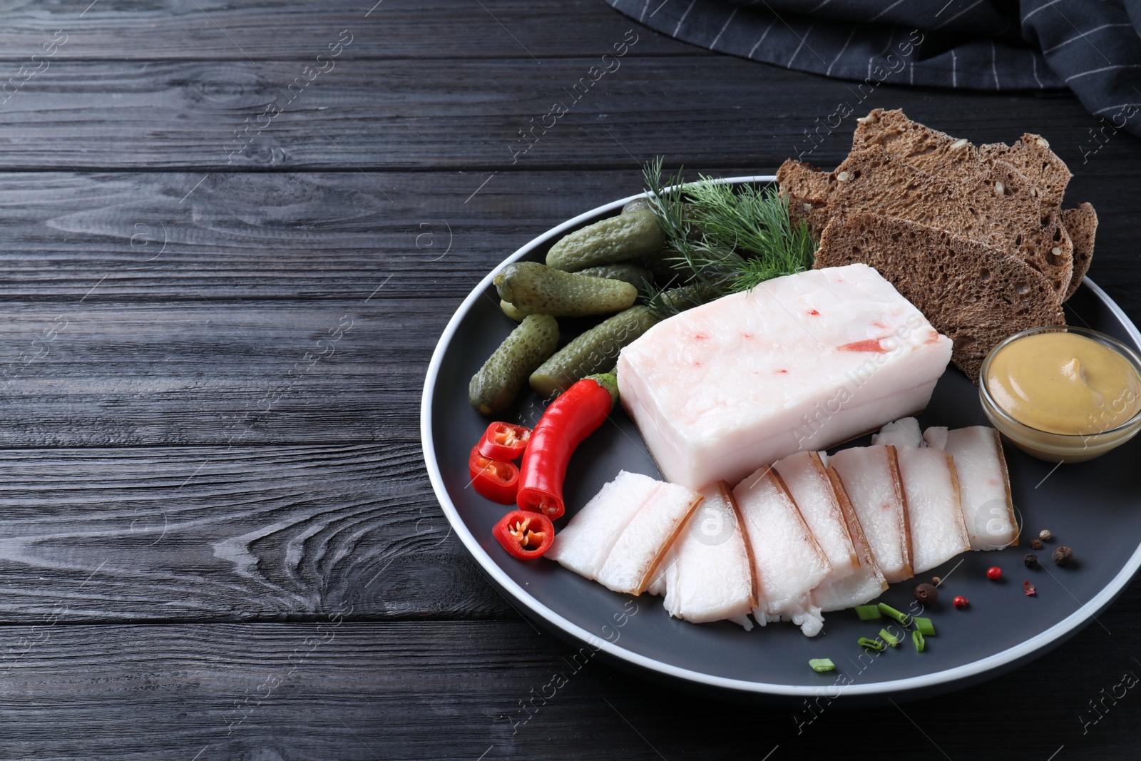 Photo of Pork fatback with spices, rye bread and pickled cucumbers on black wooden table. Space for text