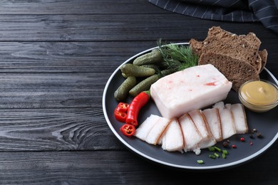 Pork fatback with spices, rye bread and pickled cucumbers on black wooden table. Space for text