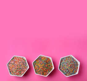 Photo of Colorful sprinkles in bowls on pink background, flat lay with space for text. Confectionery decor