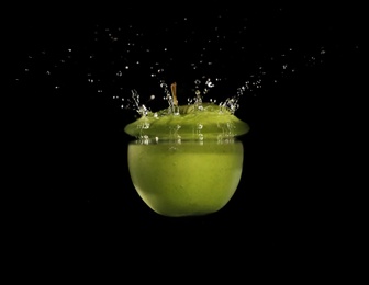 Green apple falling down into clear water against black background