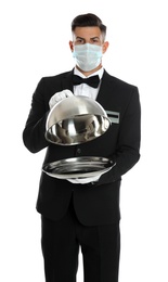 Waiter in medical face mask holding tray with lid on white background