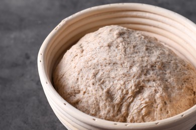 Photo of Fresh sourdough in proofing basket on grey table, closeup